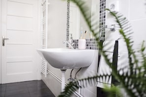 A bathroom with a white sink, a mirror, and a patterned tile backsplash. - Live Life Ermou (Athens)