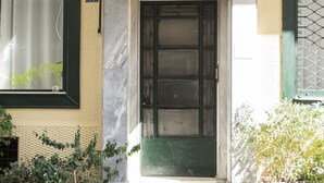 A building entrance with a green door, a number '11' sign, and potted plants on the sidewalk. - Live Life Ermou (Athens)