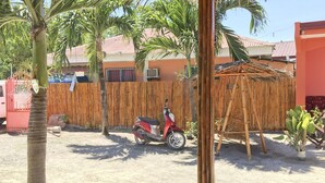 A red scooter parked in a sandy area with a bamboo structure and a wooden fence in the background.