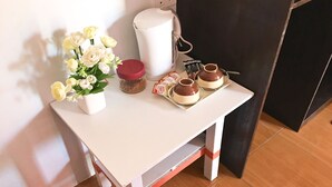 A small white table with a vase of white flowers, a red container, and two cups with saucers.