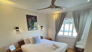 A bedroom with a large bed, wooden flooring, a ceiling fan, a window with curtains, and a wall-mounted artwork. - The Miami Beach vacation home (Miami)