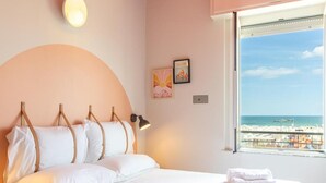Une chambre d’hôtel avec un lit, une lampe de chevet, une fenêtre donnant sur la plage et un luminaire fixé au mur.