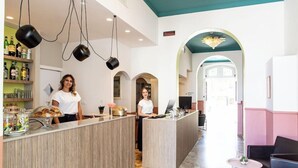 Un espace d’accueil avec un comptoir en bois, deux employés, un coin café et un espace détente avec un mur rose.