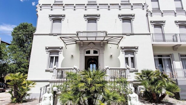 Un bâtiment blanc doté d’une entrée centrale, de balcons et de statues.