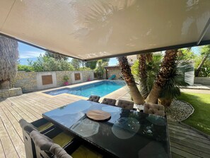 An outdoor pool area with a hot tub, wooden deck, and stone wall.