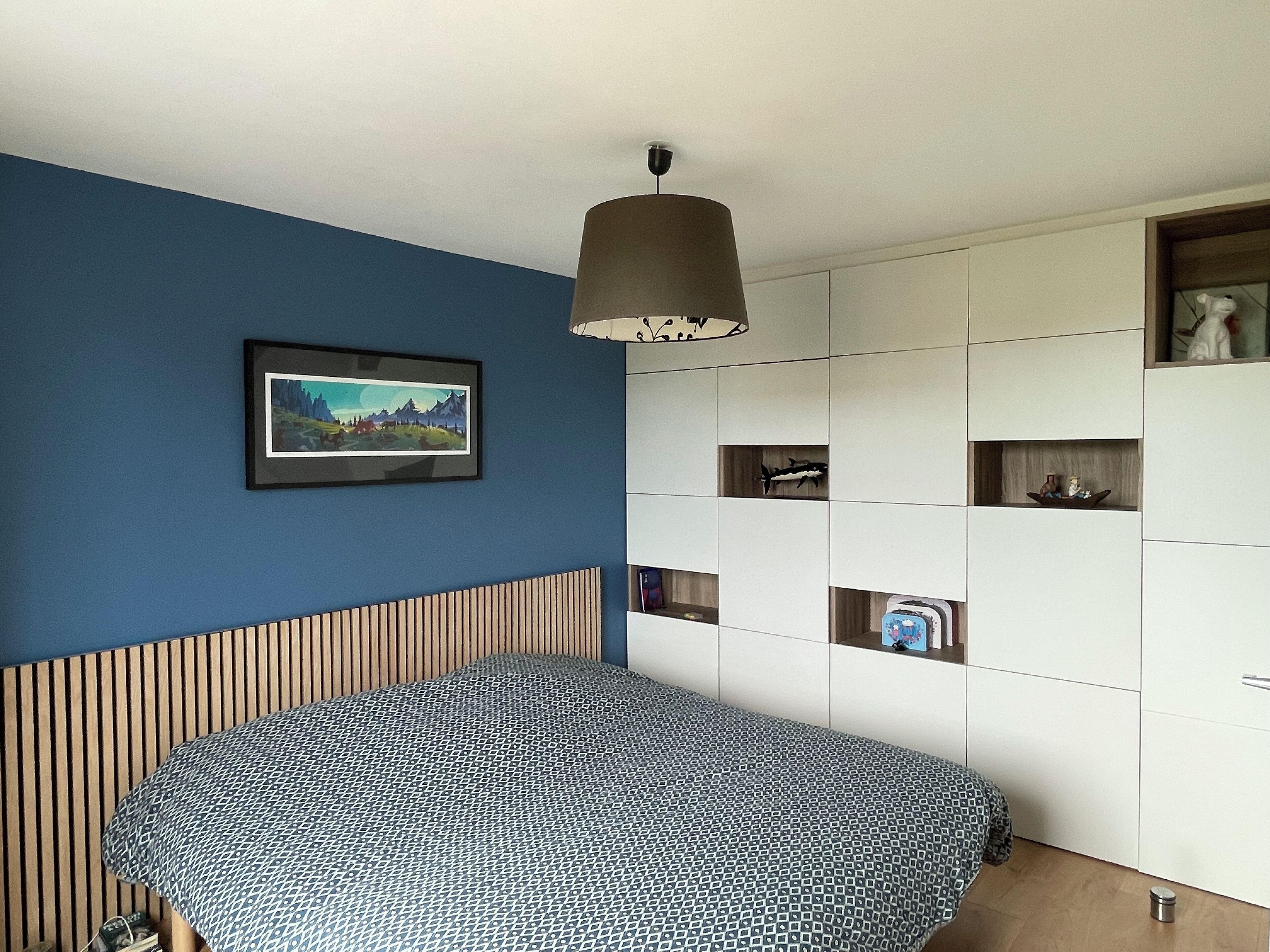 Un dormitorio con una cama, un estante en la pared con objetos decorativos y un cuadro enmarcado.