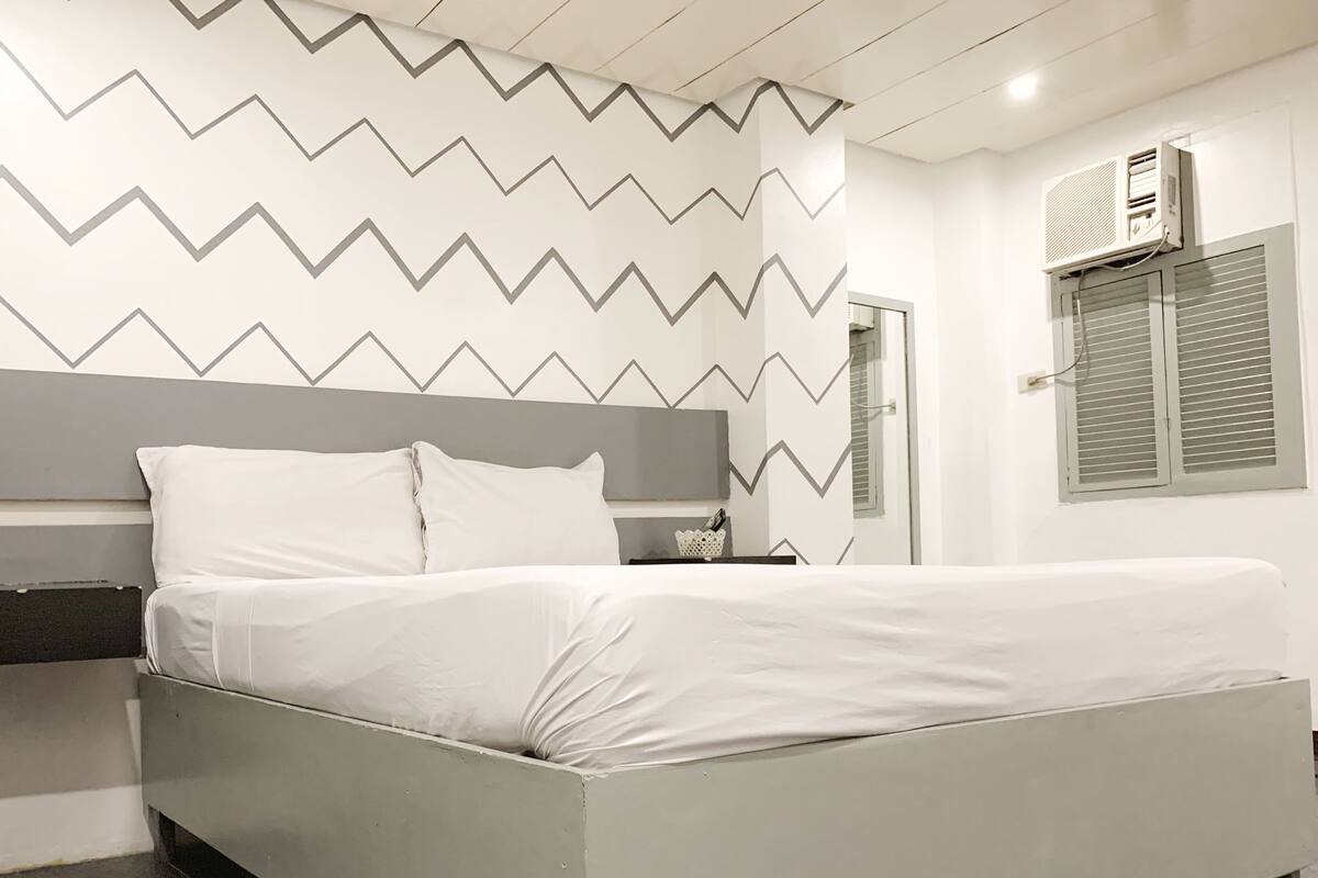 Quarto com cama, mesa de cabeceira e ar condicionado fixado na parede.
