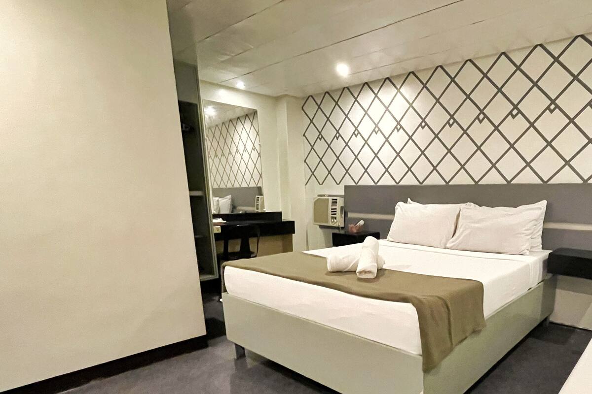 Quarto de hotel com cama, escrivaninha e espelho.