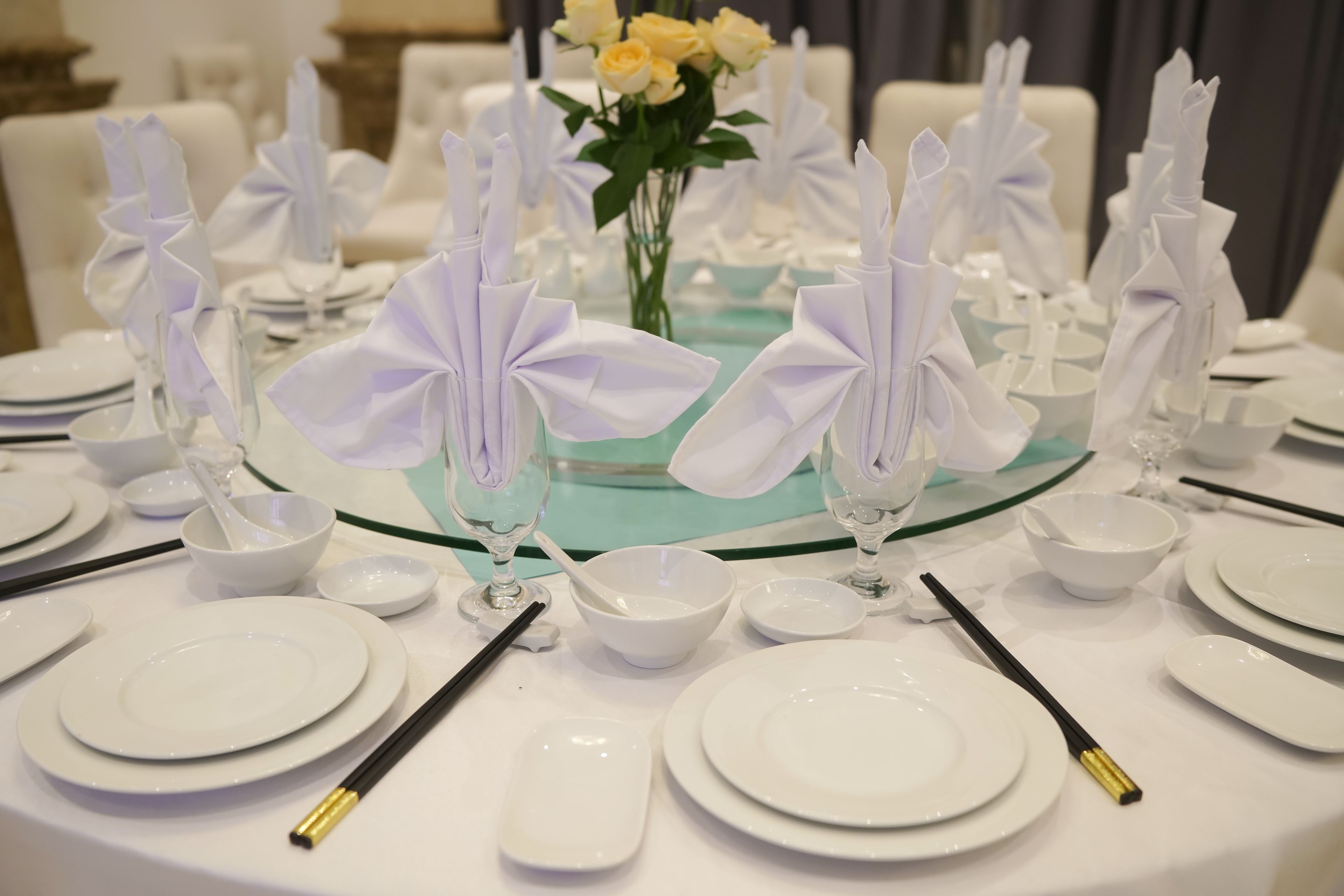 A table set for a formal event with white plates, bowls, and glasses, and napkin holders with white napkins.