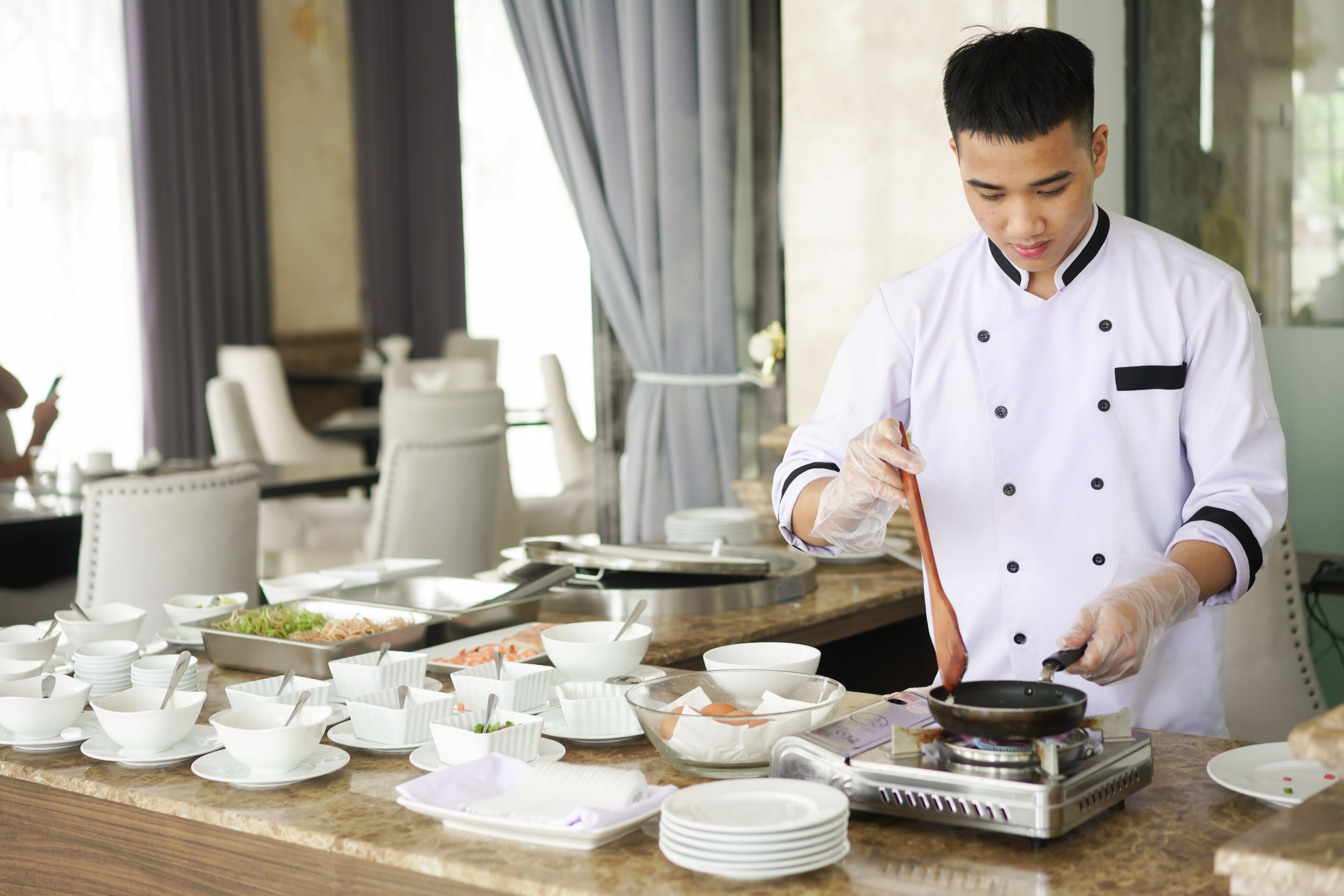 A chef preparing food in a well-lit kitchen with various dishes and utensils on the counter.