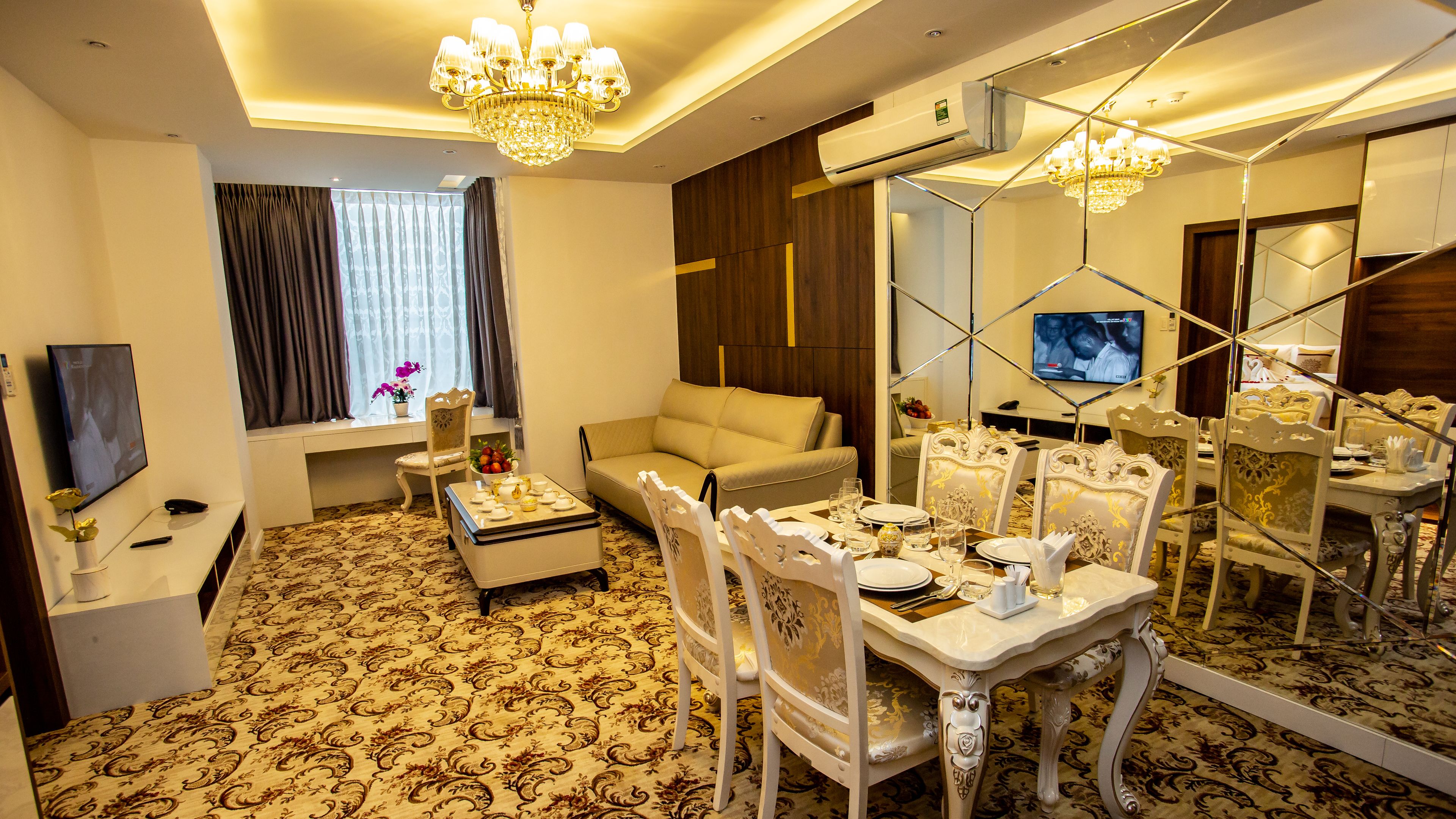 Une chambre d’hôtel bien aménagée, comprenant un coin repas, un canapé, une télévision et un grand miroir.