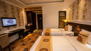 A hotel room with two beds, a TV, a desk, and a patterned carpet.