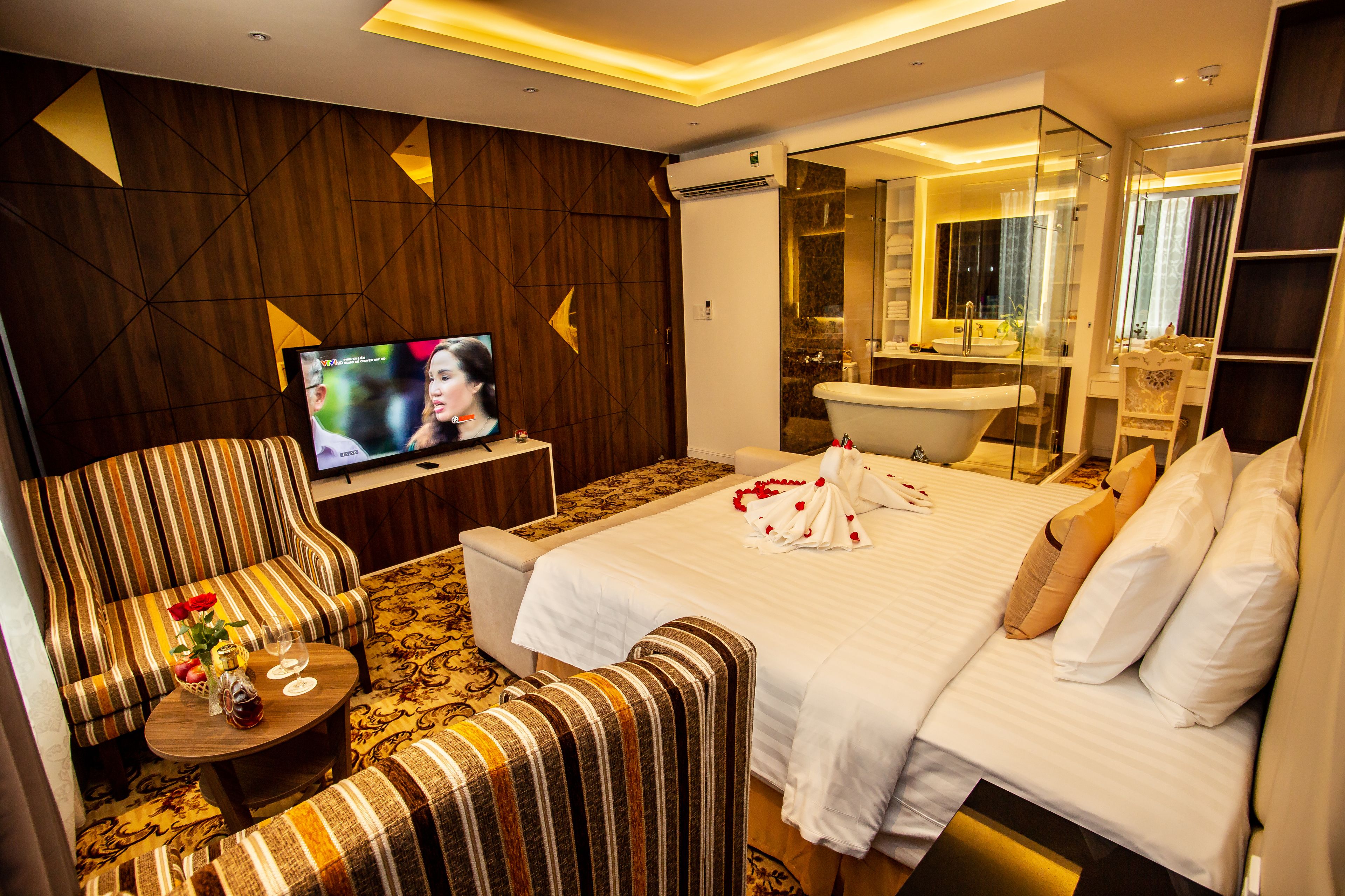 Een hotelkamer met een groot bed, een televisie, een bank en een badkamer met een douchecabine van glas.