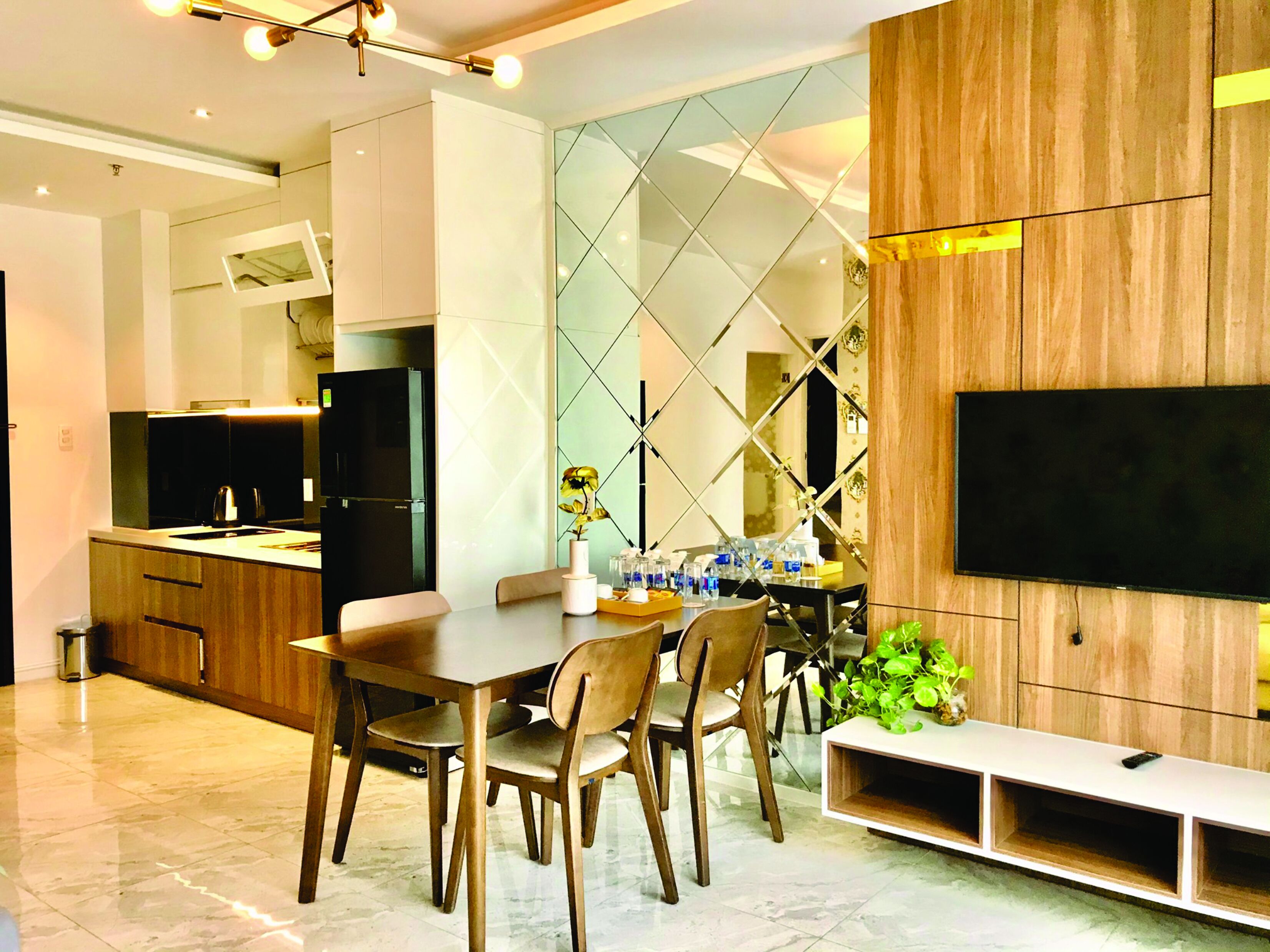 Una cocina moderna con comedor, un televisor montado en una pared de madera y una planta sobre la mesa.