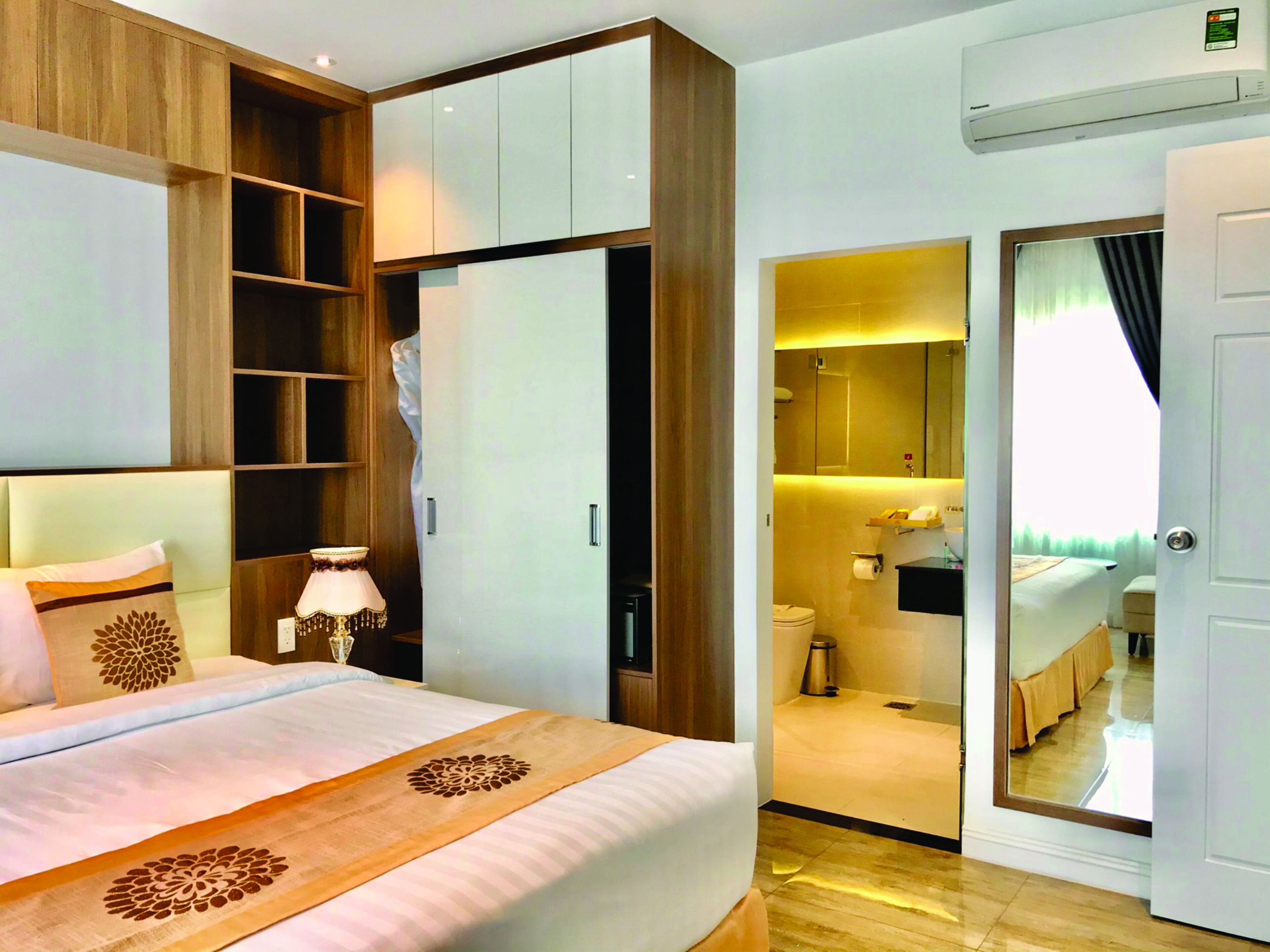 Een hotelkamer met een bed, een kledingkast, een spiegel en een zichtbare badkamer door een geopende deur.