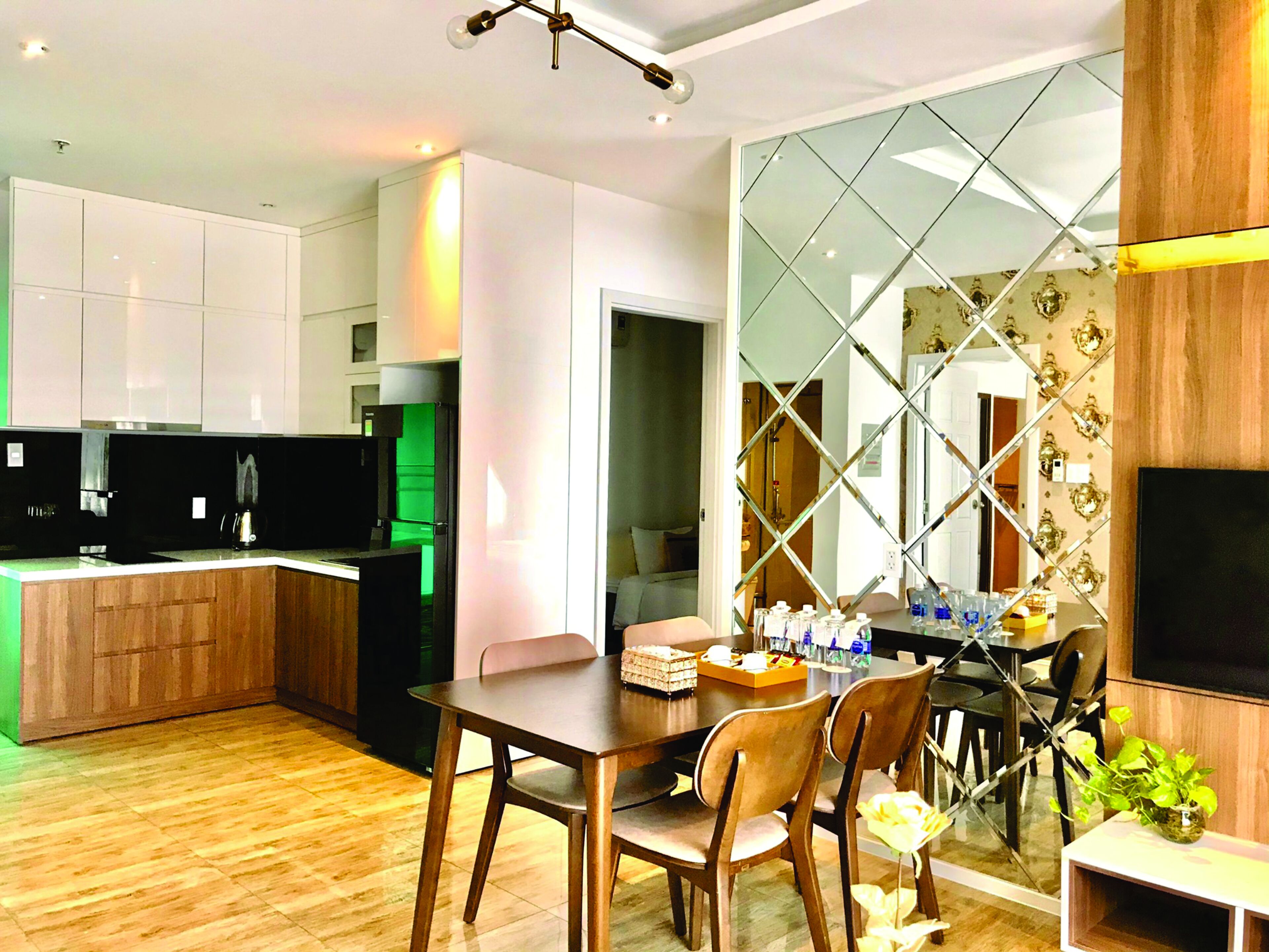 Une cuisine moderne avec des meubles en bois, un coin repas comprenant une table et des chaises, et un grand miroir orné d’un motif géométrique.