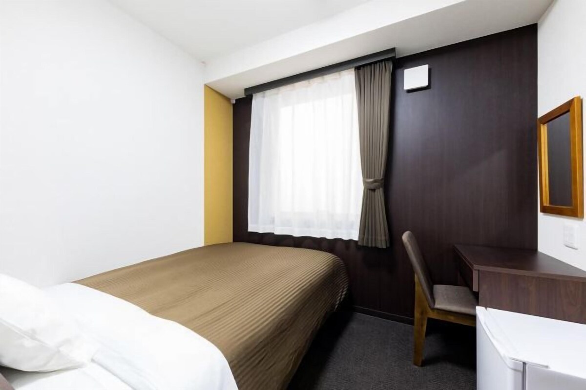 A hotel room with a bed, a desk, a chair, and a window with curtains.