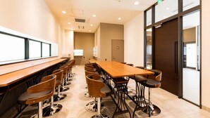 A conference room with a long table and multiple chairs, a door, and a window. - Hotel Trend MikawaAnjo (Anjo)