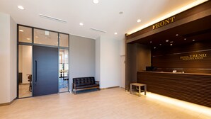 A hotel reception area with a modern design, featuring a reception desk, a sofa, and a glass door leading to another room. - Hotel Trend MikawaAnjo (Anjo)