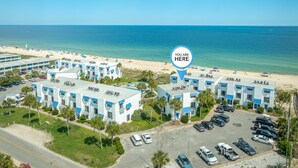 Une vue aérienne d'un hôtel composé de plusieurs bâtiments, avec un parking et une plage en arrière-plan.