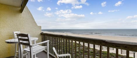 A balcony with white chairs and a table overlooking a beach.