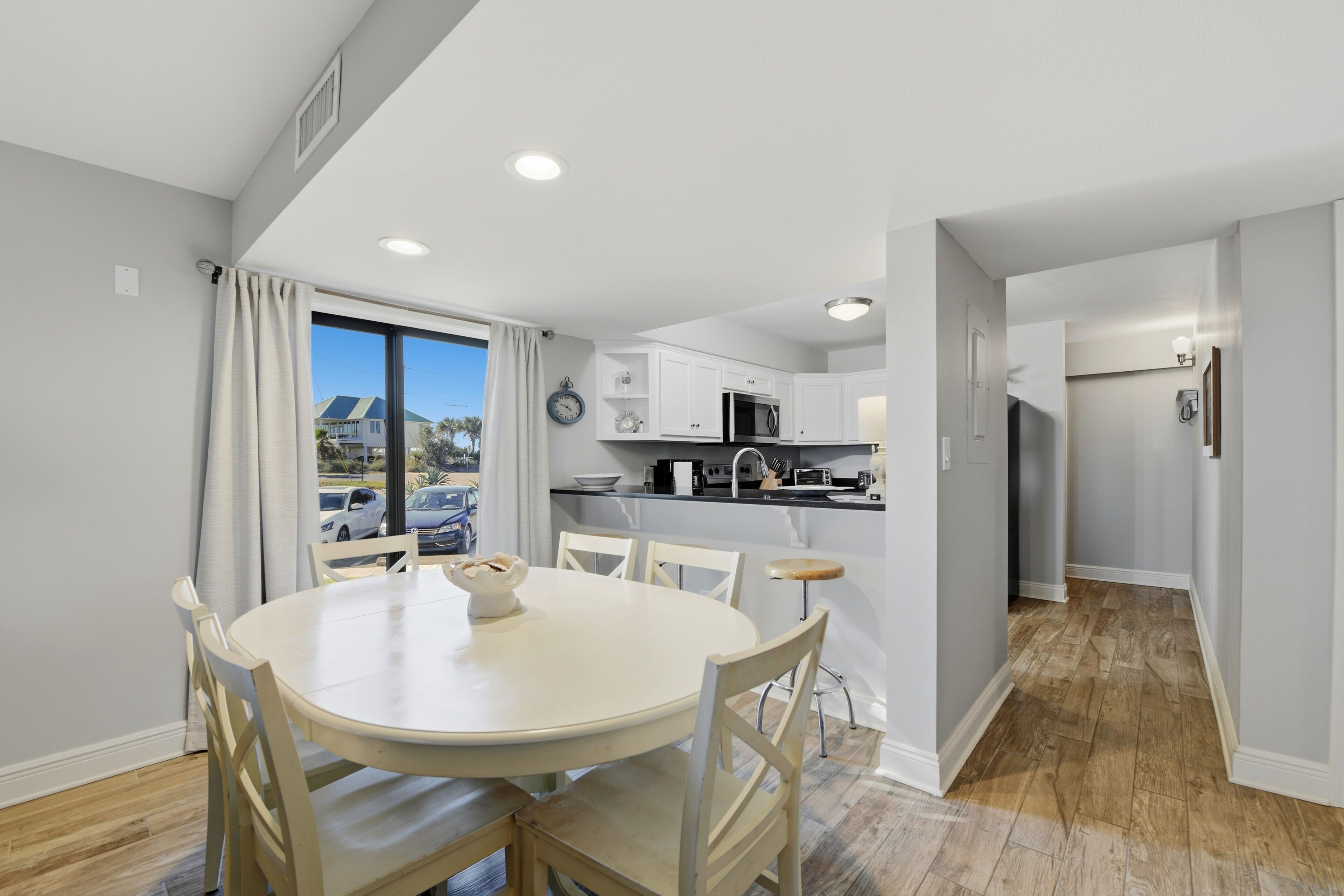 A modern kitchen with white cabinets, a microwave, and a sink. There is a dining area with a round table and chairs.