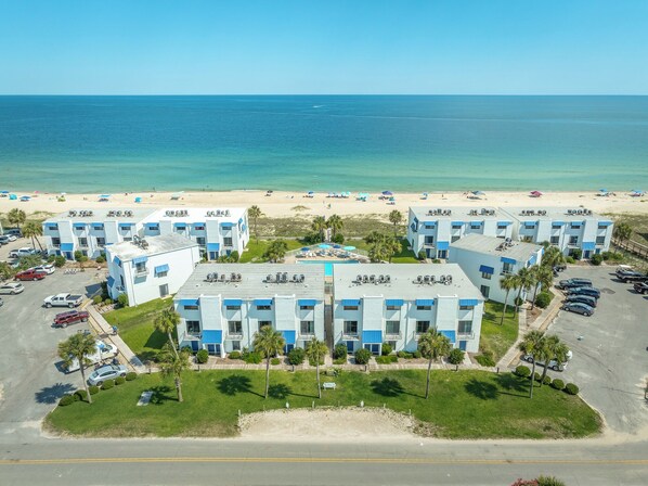 A beachfront hotel with multiple blue and white buildings, a parking lot, and a sandy beach with umbrellas. - EMBRACE NATURAL BEAUTY with elegant refinement. Exquisite decor emulates a tropical paradise. (St. George Island)