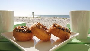 Une assiette avec trois beignets et deux tasses blanches sur une table verte, sur une plage.