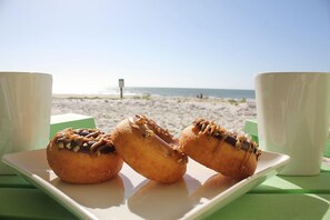 A plate with three donuts and two white cups on a green table at a beach. - EMBRACE NATURAL BEAUTY with elegant refinement. Exquisite decor emulates a tropical paradise. (St. George Island)
