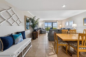 A spacious living area with a sofa, dining table, and chairs. There is a large window providing a view of the outdoors.
