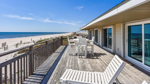 A wooden deck with a white table and chairs overlooking a beach.