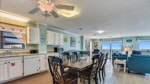 A spacious kitchen with white cabinets, a dining area with wooden chairs, and a view of the ocean through large windows.