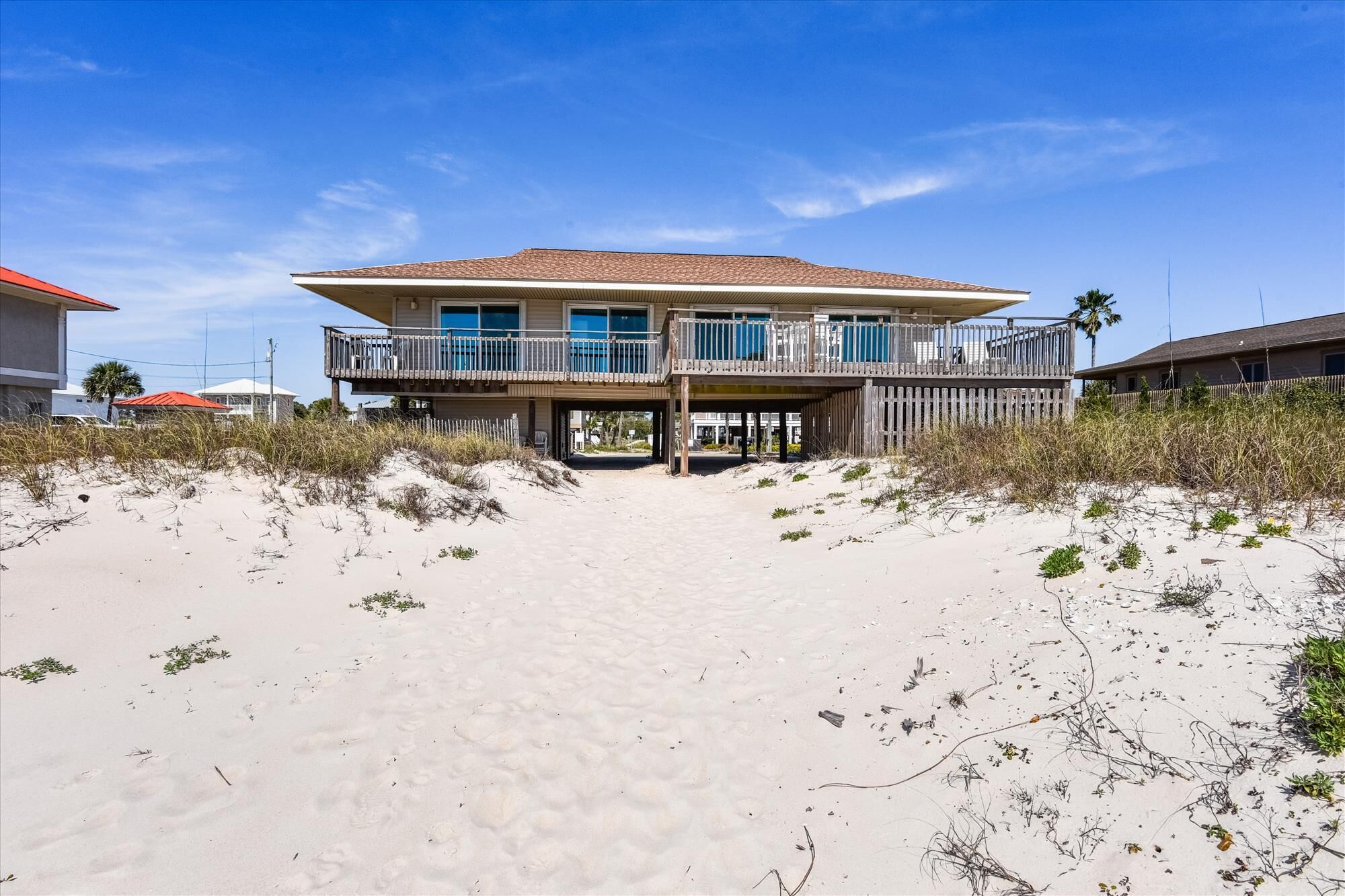 A beachfront house with a two-story balcony, a covered entryway, and a sandy beach in the foreground.