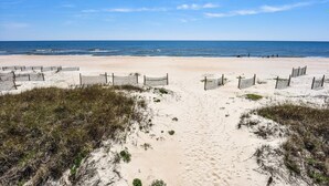 A sandy beach with a wooden fence and beach chairs.