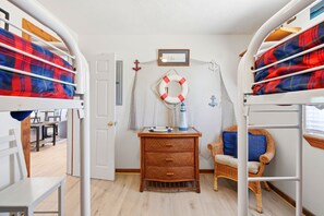 A room with bunk beds, a wicker chest of drawers, a wicker chair, and a life preserver hanging on the wall.