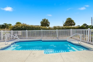 A rectangular swimming pool with a white fence and two white chairs.