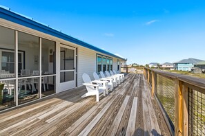 A wooden deck with white chairs and a glass-enclosed room with a blue roof.