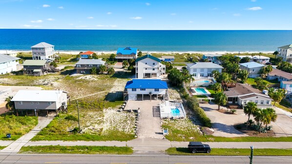 A coastal residential area with multiple houses, a swimming pool, and a beach in the background.
