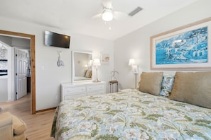 A bedroom with a bed, a television, a painting, and a door leading to another room.