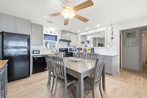 A modern kitchen with a black refrigerator, wooden chairs, a dining table, and a ceiling fan.