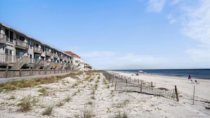 Hotel aan het strand met meerdere balkons, een zandstrand op de voorgrond en de oceaan op de achtergrond.