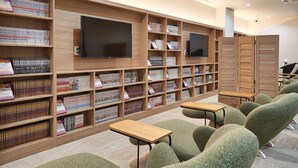 A library with wooden shelves, a flat-screen TV, and green upholstered chairs. - CABIN & HOTEL ReTIME - Hostel (Naha)