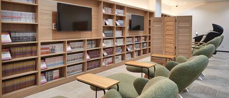 Una biblioteca con estanterías de madera, un televisor de pantalla plana y sillones tapizados en verde.