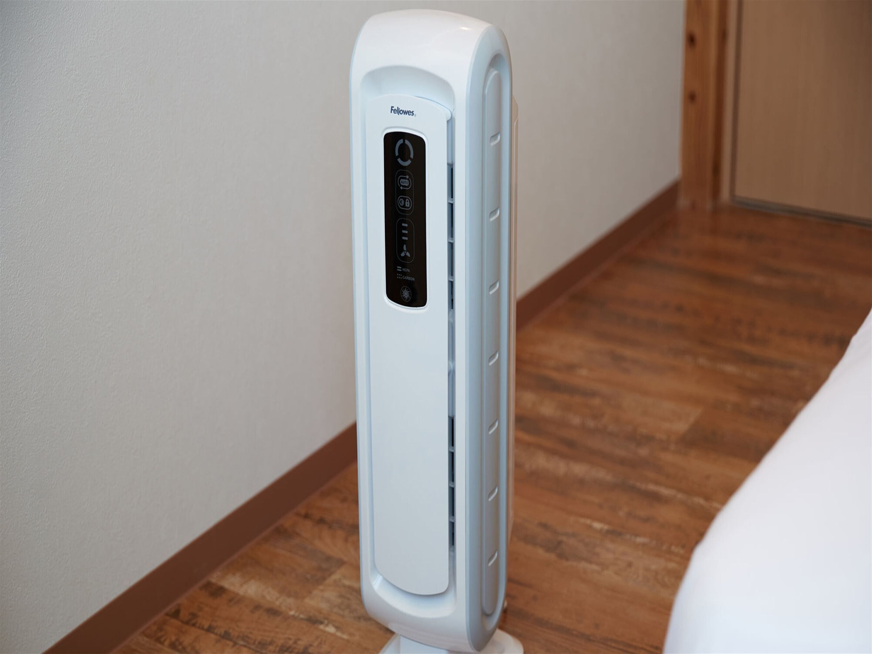 A white portable heater with a control panel, standing on a wooden floor next to a white wall.
