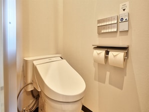 Inodoro con botón de descarga, dispensador de toallas de papel y panel de control del calentador de agua.