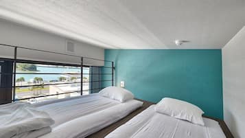 A hotel room with two single beds, a teal accent wall, a large window with a view of the city, and a security camera on the ceiling.