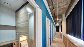 A modern hotel corridor with wooden and blue walls, a carpeted floor, and a row of rooms with beds and windows. - CABIN & HOTEL ReTIME - Hostel (Naha)
