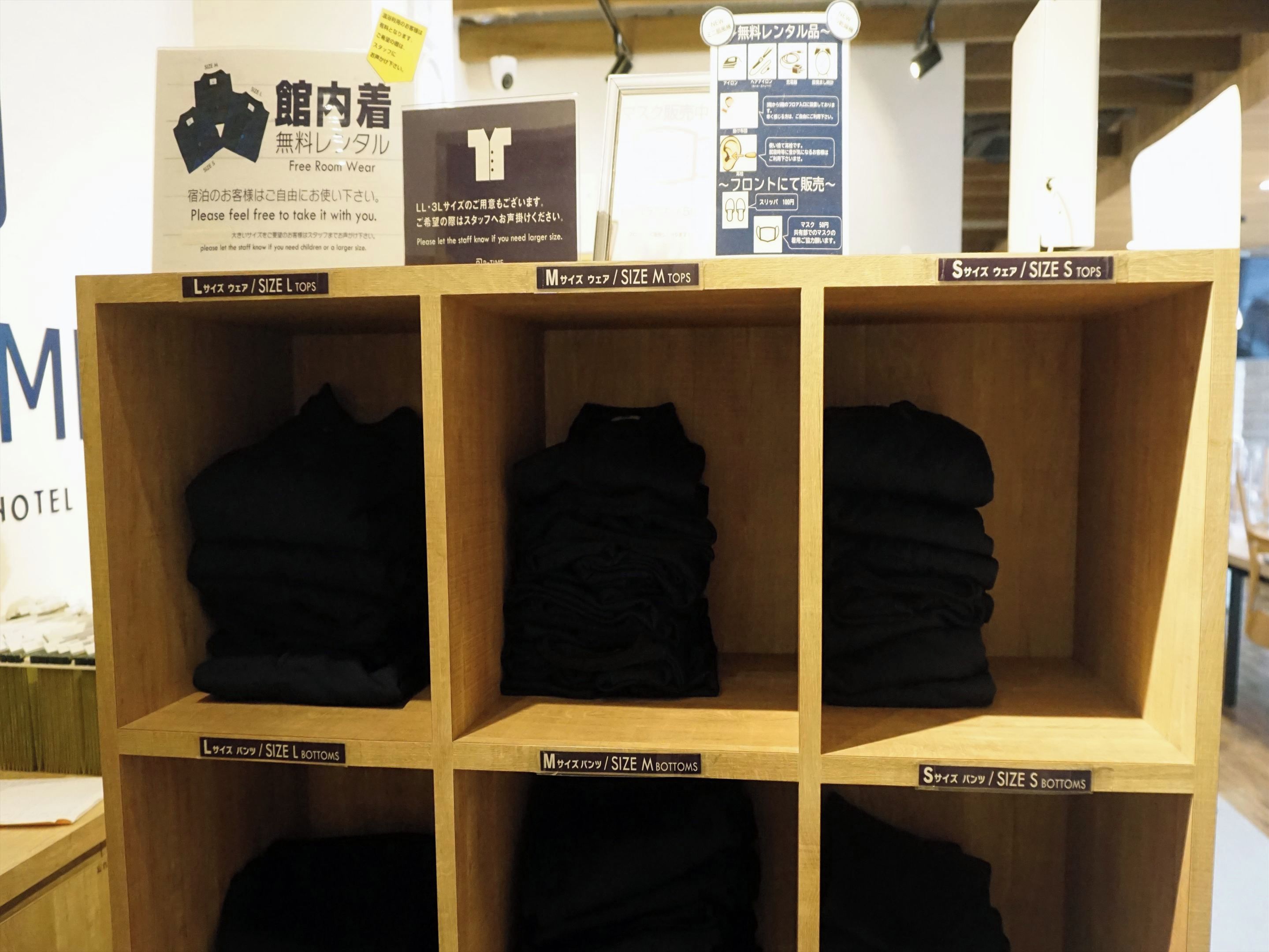 A hotel room with wooden shelves displaying folded clothes in sizes L, M, and S.