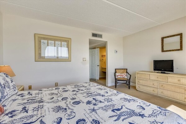Una camera da letto con un letto, una televisione su un comò, una sedia e una porta che dà su un'altra stanza.