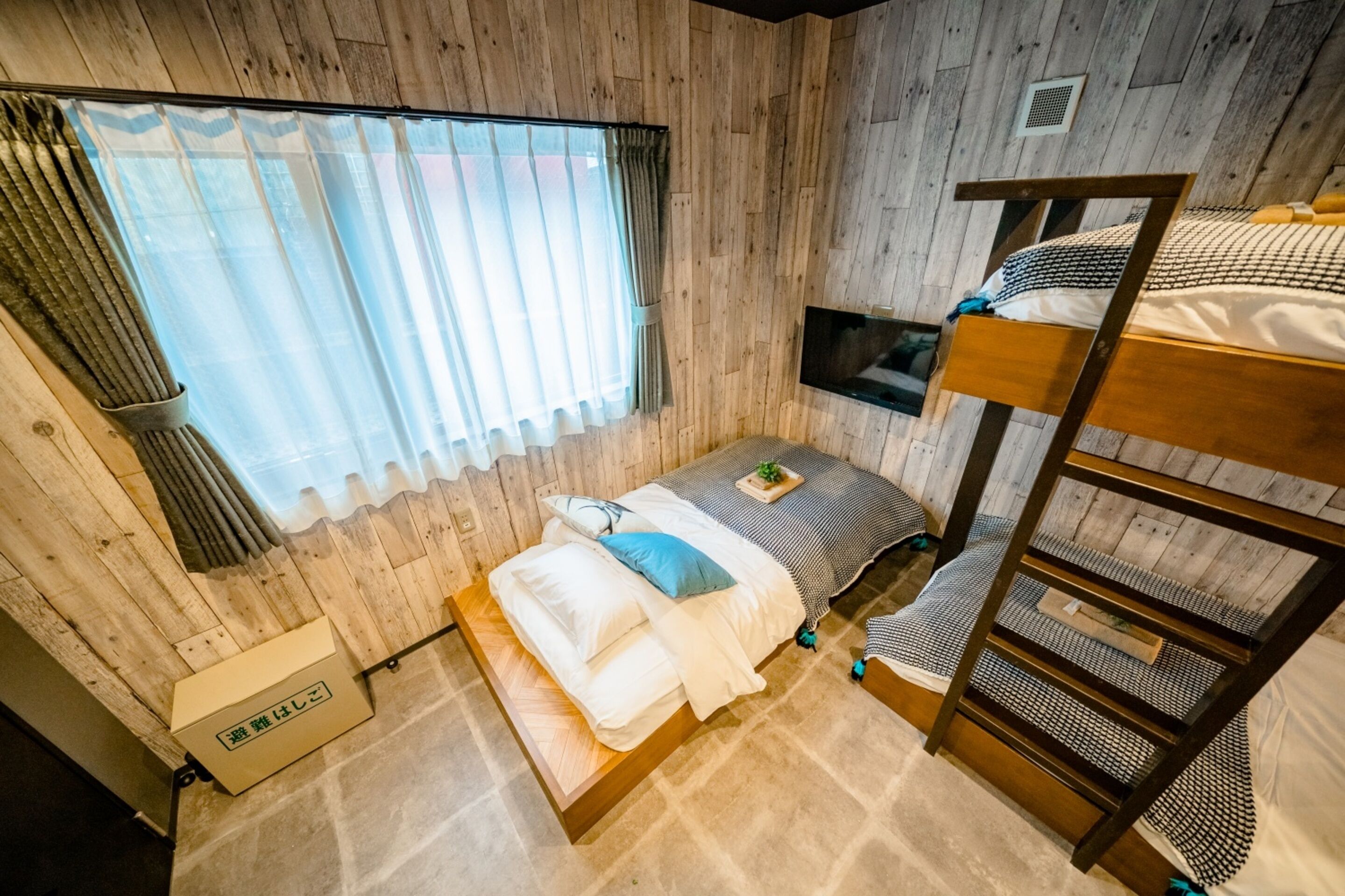 A bunk bed room with a wooden wall, a window with curtains, a television, and a small bedside table.